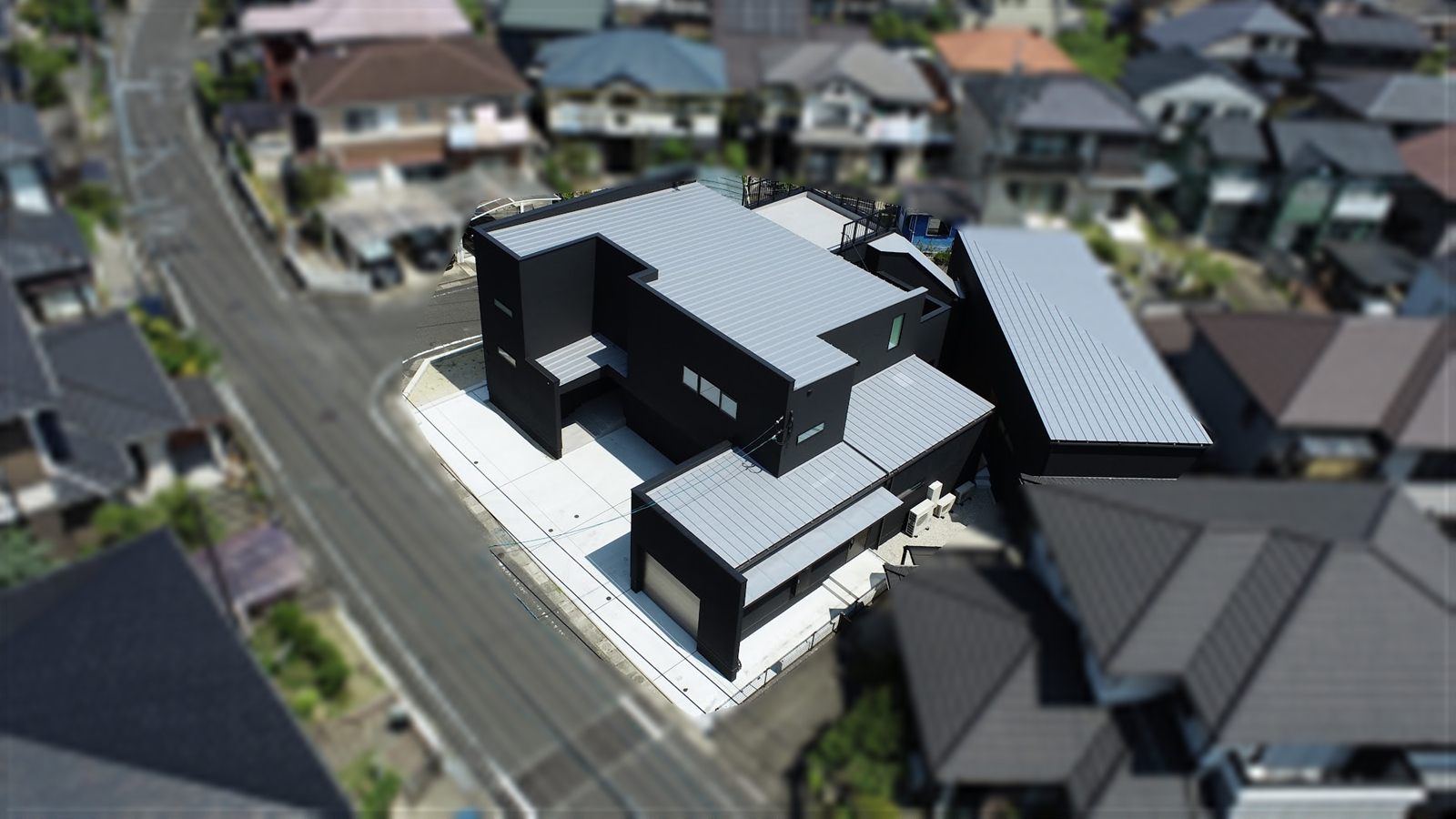 上空から見た、曲がる道路の角に沿って建つ母屋と離れ
